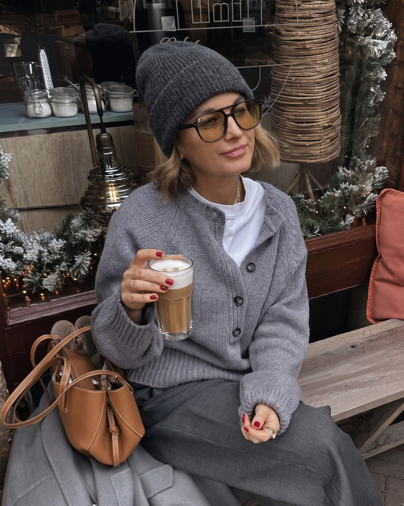 The Alashan Cashmere-Blend Beanie in Dark Grey, worn at a cafe table with a grey cardigan