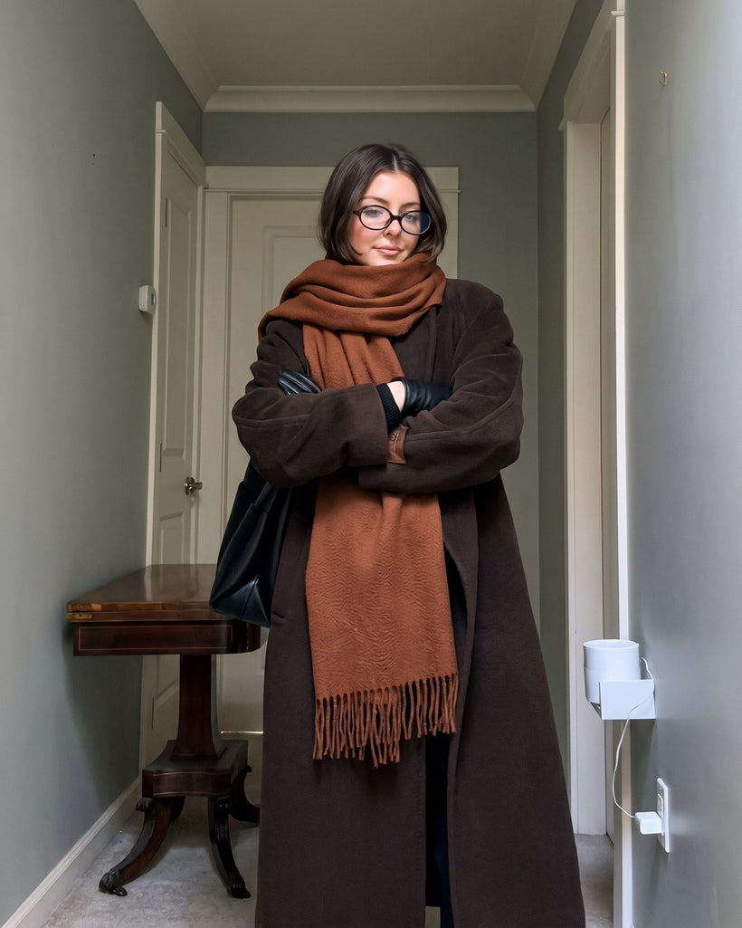 The Dune 100% Cashmere Scarf in Bronze, worn knotted over a long brown coat