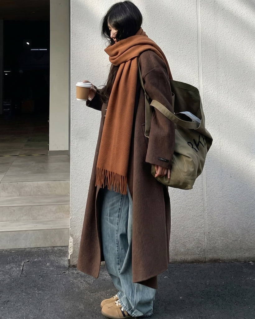 The Dune 100% Cashmere Scarf in Bronze, worn hanging long over a brown coat with jeans