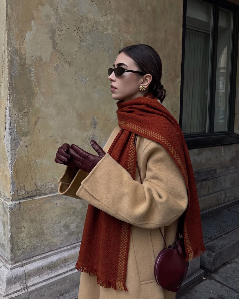 The Herringbone Wool Scarf in Burgundy, worn over one shoulder with a camel coat