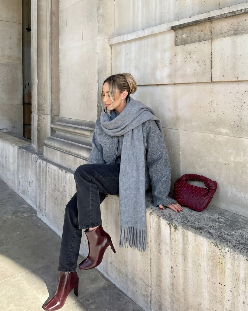 The Brushed Lambswool Long-Scarf in Grey, worn looped once, seated on a stone ledge