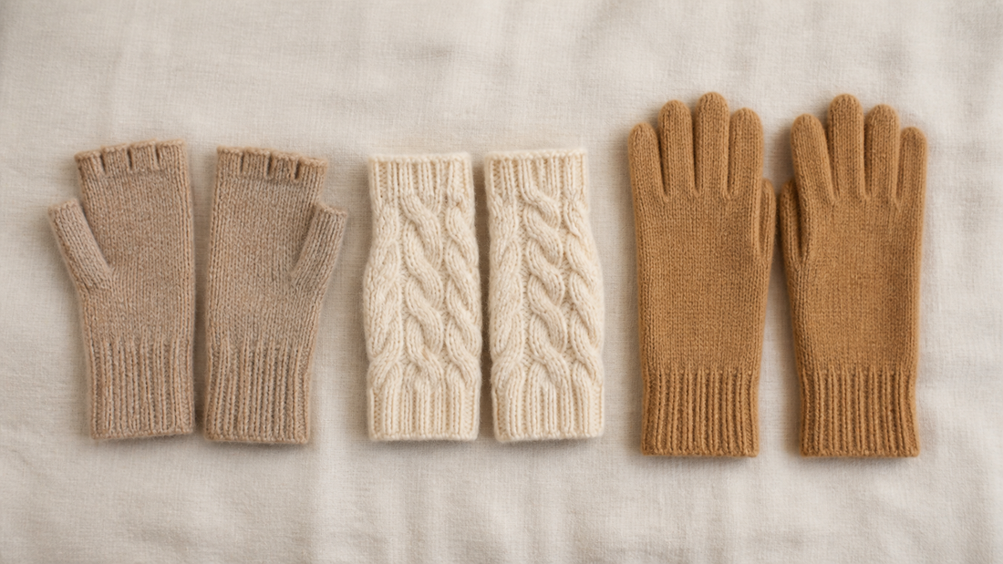 Flat lay of cashmere fingerless gloves, cable-knit wrist warmers and full knitted wool gloves in a row on cream linen
