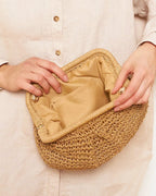 Camel straw bag with brass chain catching evening light — lifestyle shot