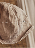 Wildfool Washed Linen Docker Cap in White — flat lay on natural linen surface
