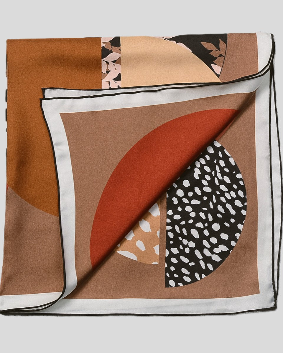 Cream and bold color-blocked scarf tied at neck, geometric design visible against neutral sweater