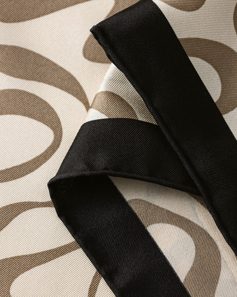 Cream silk scarf tied loosely at neck showing deep navy border and abstract movement