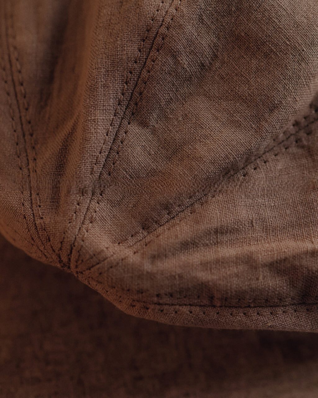 Macro close-up of the washed linen weave and topstitched panel seams on the Wildfool Docker Cap in Espresso