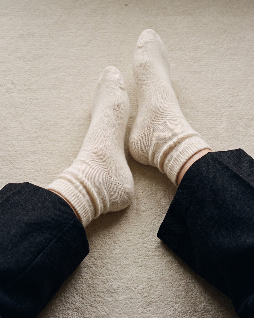 The 100% Cashmere Bed Socks in Beige, worn on a cream carpet with dark trousers
