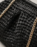 Camel straw bag with brass chain catching evening light — lifestyle shot