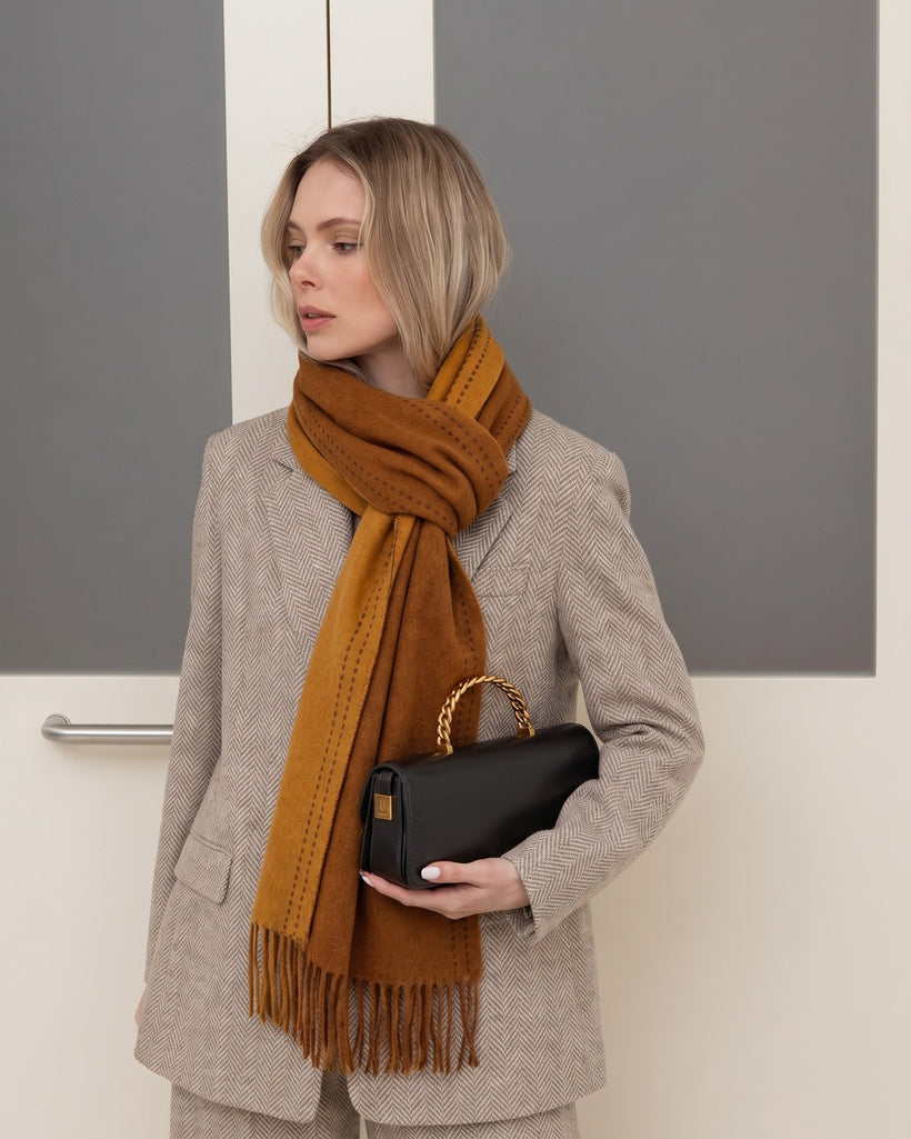 The Reversible Topstitch Scarf in Camel, worn knotted over a grey blazer