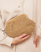 Camel straw bag with brass chain catching evening light — lifestyle shot