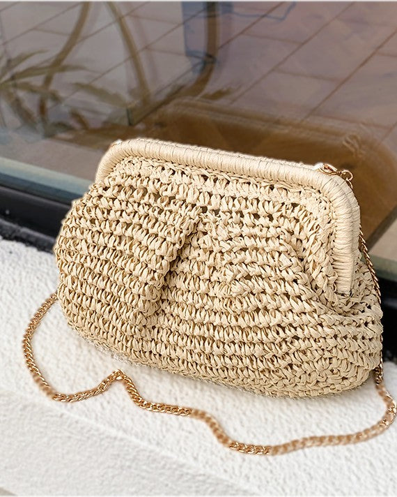 Camel straw bag with brass chain catching evening light — lifestyle shot