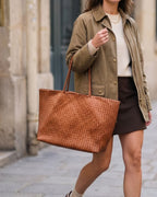The Heritage Woven Leather Tote in Cognac, carried on the shoulder