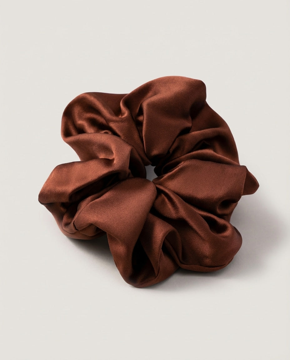 Loose silk scrunchie draped on a marble vanity beside a hairbrush — lifestyle shot