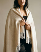 Wildfool herringbone cashmere-blend throw in oat — full flat lay on a leather sofa