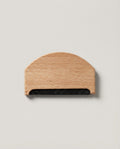 Hand using the beechwood comb to lift pills off a folded cashmere sweater
