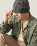 Wildfool cable-knit wool fisherman beanie in oat — front view on linen background