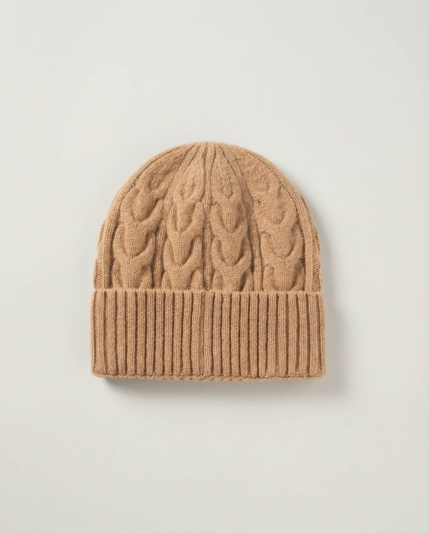 Cable-knit wool beanie folded flat next to a leather journal — still life