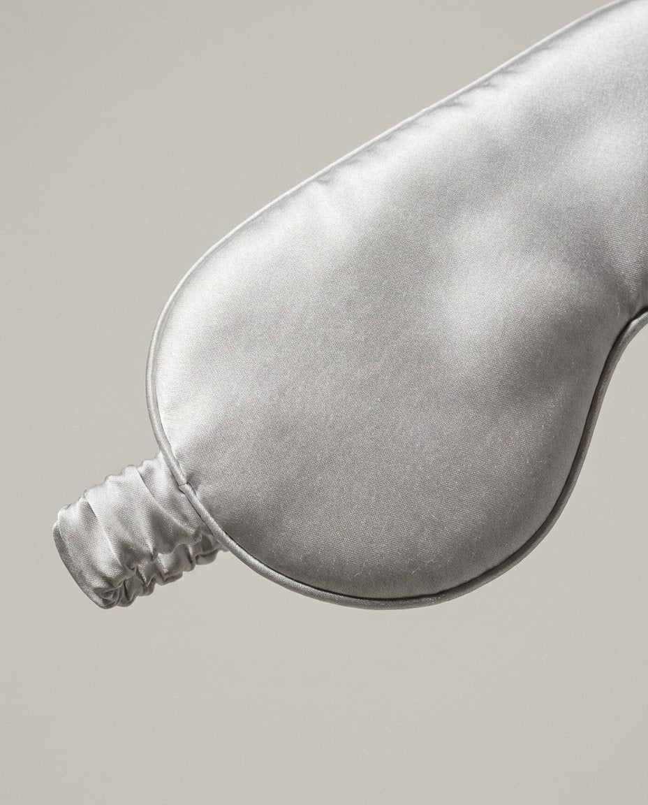 Wildfool 22-momme silk sleep mask in hand for scale, beside a coffee cup