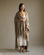 Model sitting with blanket-wrap over both shoulders reading — lifestyle indoor shot